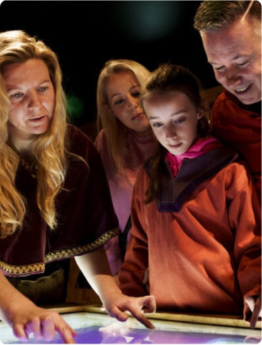 Four people, including a child and three adults, stand closely together and interact with a glowing touchscreen display, looking engaged and curious.