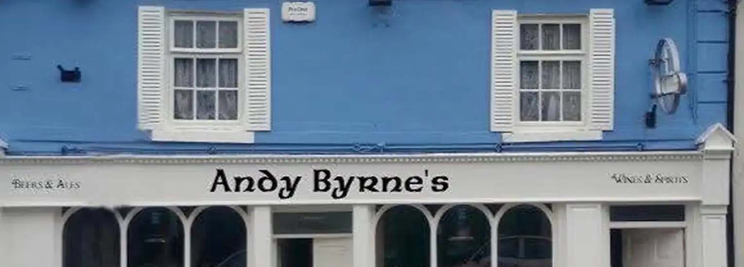 A blue building with white window shutters and a shopfront sign that reads "Andy Byrne's" above arched windows; smaller text on the sign says "Wines & Ales" on both sides.