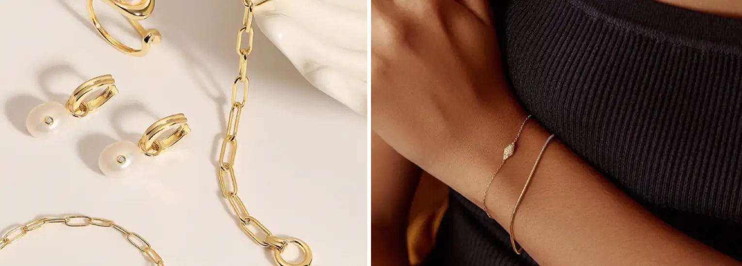 Gold jewellery including a chain necklace, hoop earrings with pearls, and a ring, displayed on a light surface; on the right, a person wearing a delicate gold bracelet rests their hand on their torso, dressed in dark fabric.