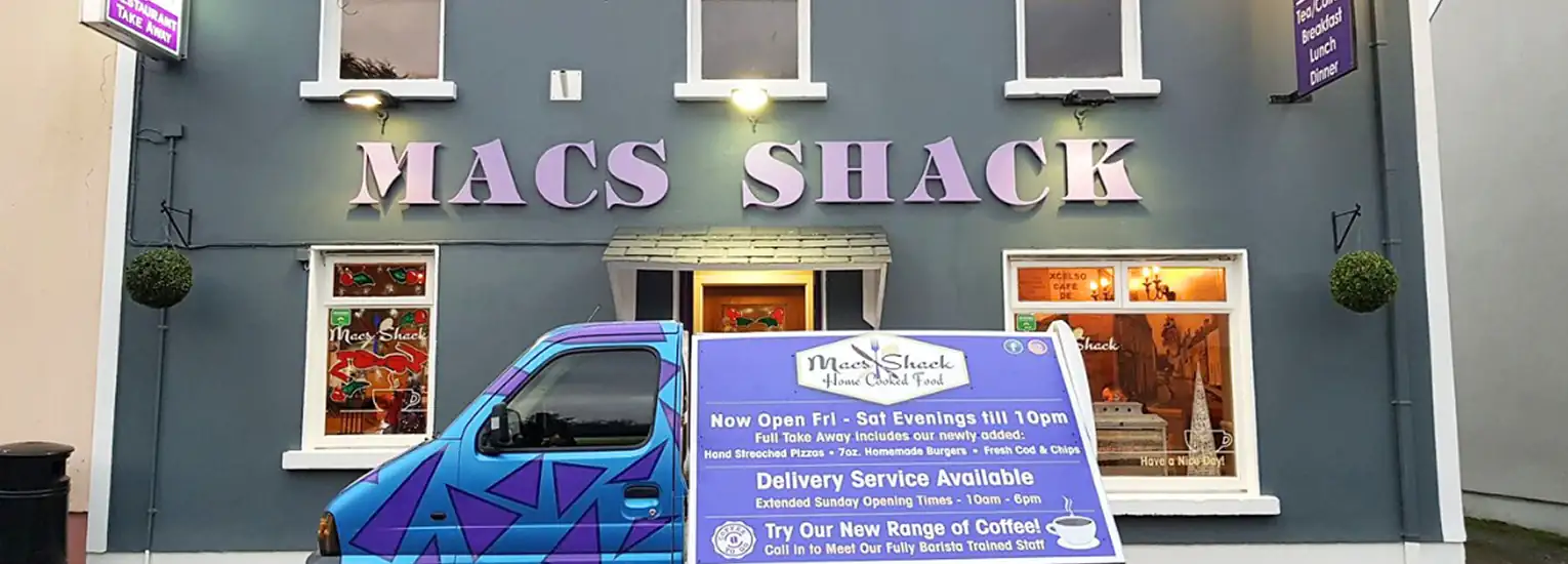 Exterior view of Macs Shack restaurant with large purple sign, a blue delivery van parked in front, and a board displaying information about opening times, delivery service, and coffee offerings.