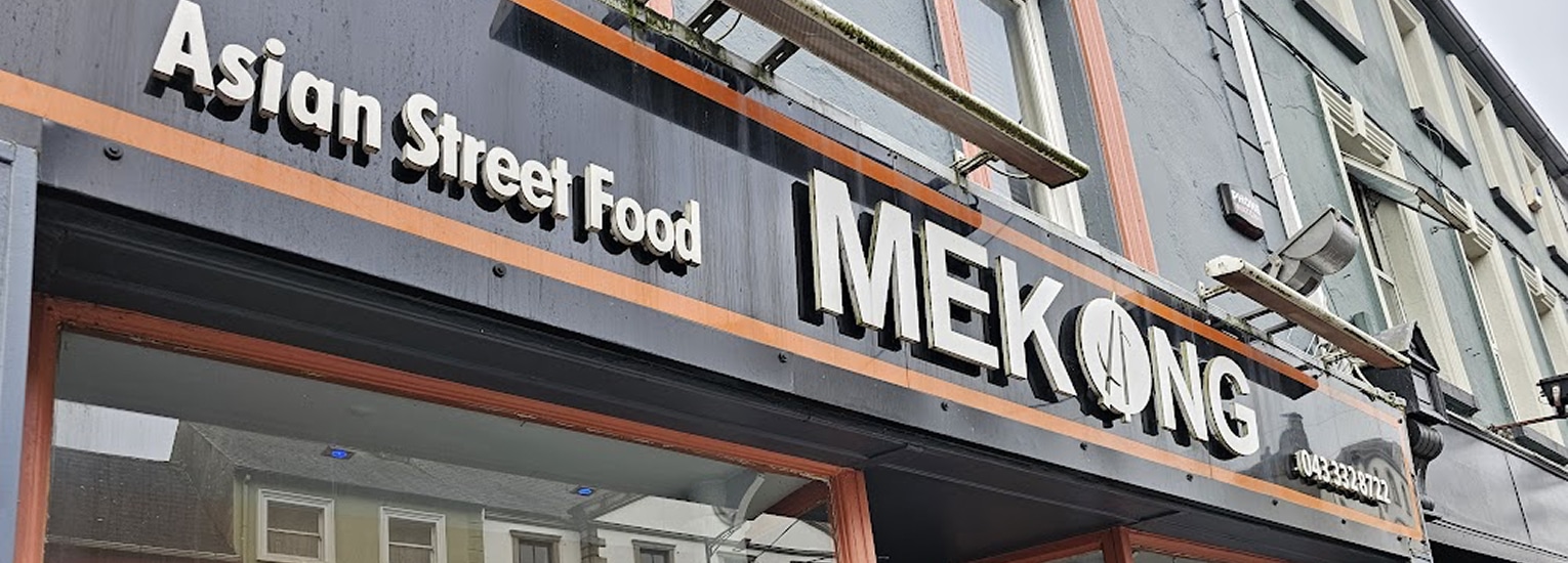 A restaurant sign reading "Asian Street Food MEKONG" is shown on the exterior of a building, with part of the street and other buildings reflected in the windows below.