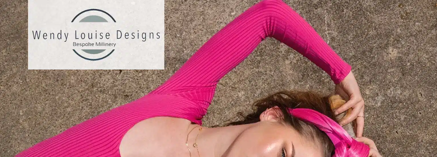 A woman in a bright pink top and matching headband lies on a concrete surface. The logo for "Wendy Louise Designs Bespoke Millinery" appears in the top left corner.