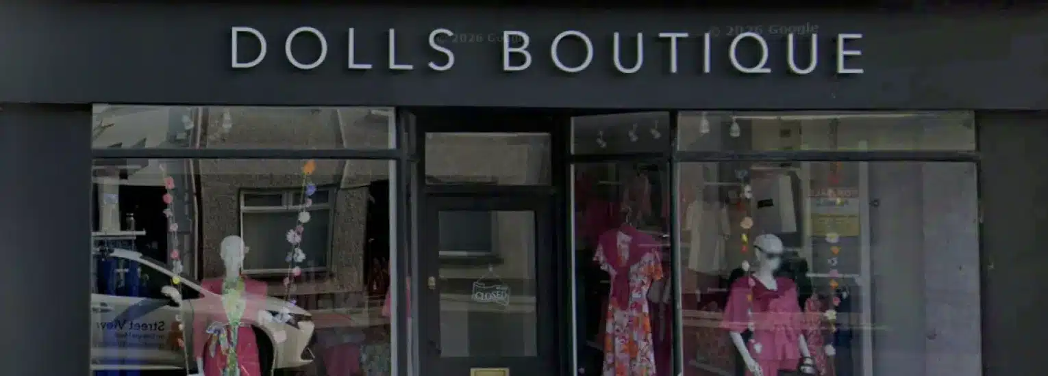 Shopfront of Dolls Boutique with large white signage and two display windows showing mannequins dressed in colourful clothing.