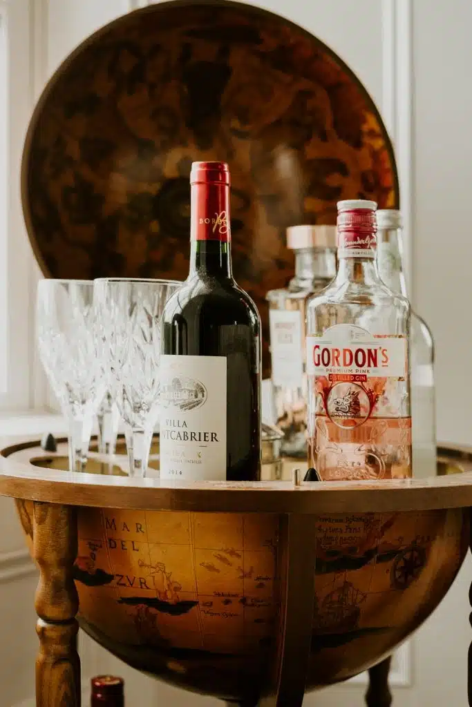 A globe-shaped drinks trolley open to reveal bottles of wine and gin, surrounded by crystal wine glasses and other spirits bottles, with a vintage world map design inside the globe.