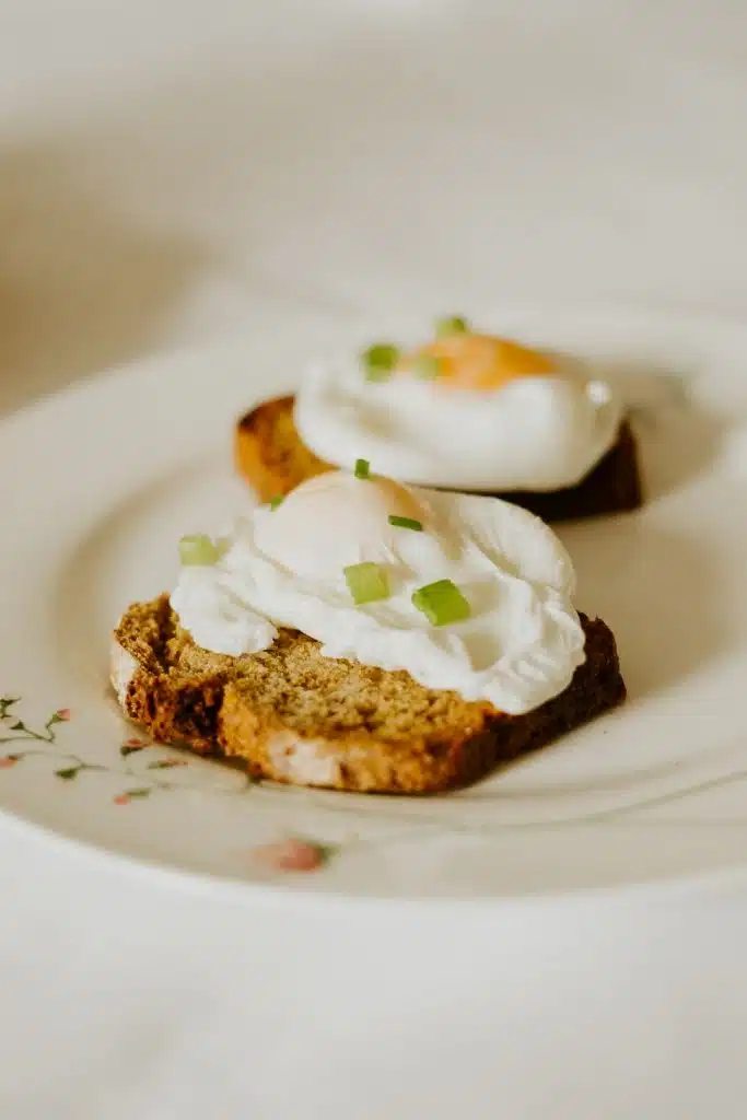 Two slices of bread topped with poached eggs and garnished with chopped spring onions, served on a white plate with a floral design.