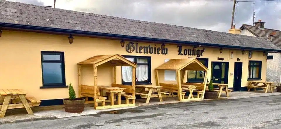 A single-storey building labelled "Glenview Lounge" has outdoor wooden picnic tables and covered seating areas on the pavement in front. The exterior walls are beige with dark trim and windows.