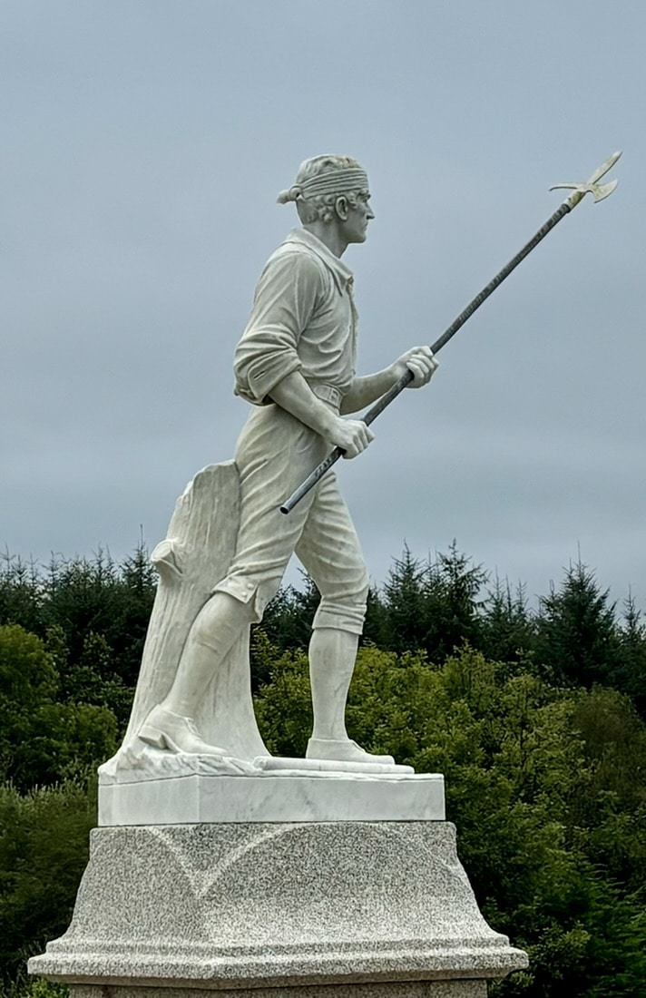 A white statue of a man in colonial attire holding a spear, standing on a granite plinth with trees and a cloudy sky in the background.